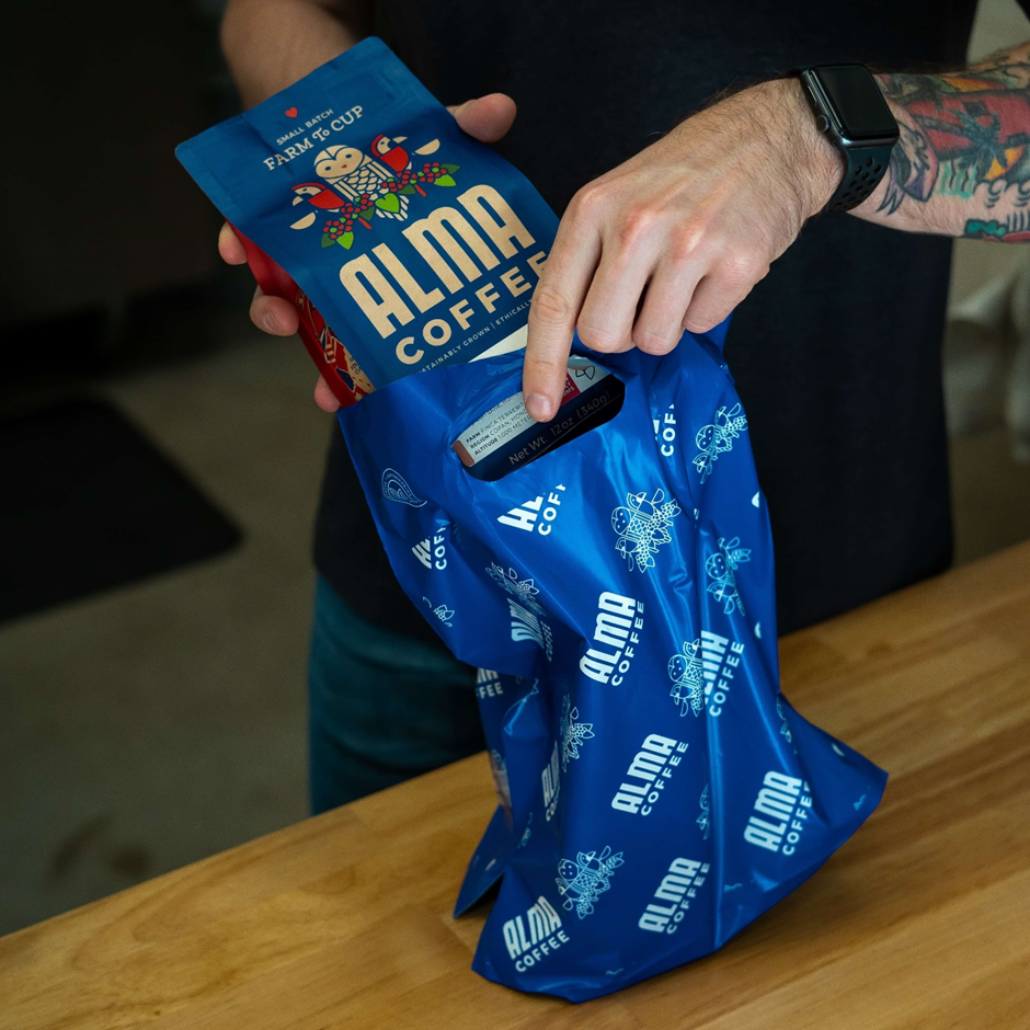 Alma Coffee's blue die-cut handle bag being packed by a set of two hands.